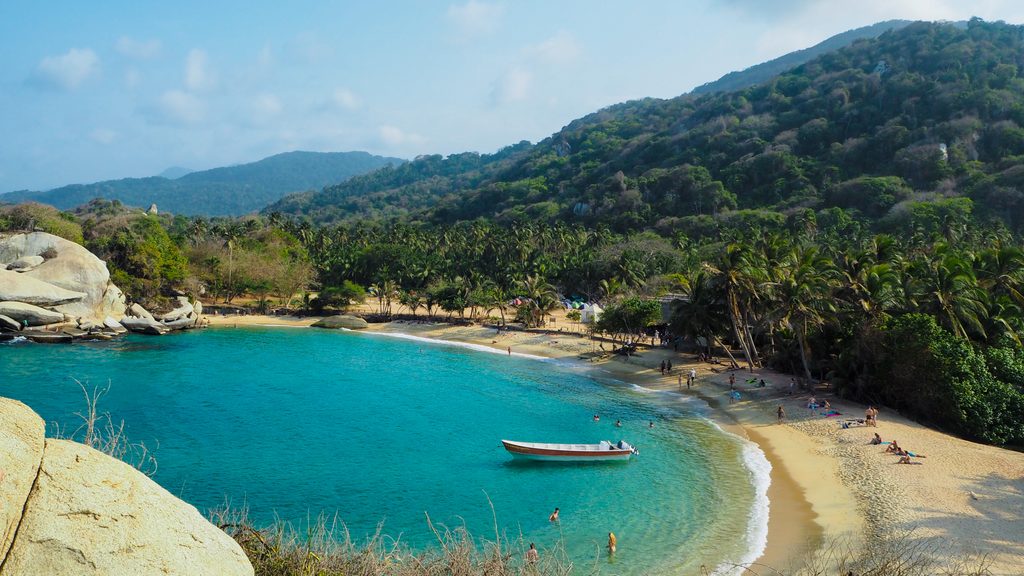An overhead view of the turquoise waters of a beach in Tayrona National Park, surround by lush forest